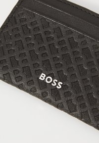 Titular de carduri negru, realizat dintr-un material texturat, cu un logo "BOSS" embosat, un model geometric și două sloturi pentru carduri în partea superioară.