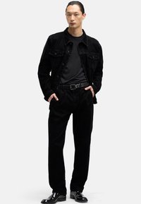 Czarna kurtka sztruksowa i pasujące spodnie, zestawione z czarnym t-shirtem i paskiem. Całość uzupełniają połyskliwe czarne buty.