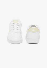 Zapatillas blancas con parte superior de cuero suave, acentos amarillos en los costados, puntera redonda, suela de goma plana y logo en relieve en el talón.