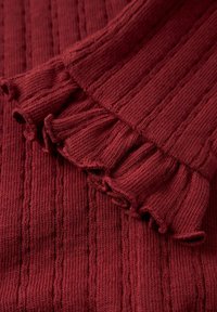 Ribbed burgundowy materiał z falbaniastym wykończeniem. Wyróżnia się pionowymi liniami tekstury i miękkim splotem. Idealny do noszenia na warstwy lub na co dzień.