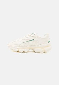 Chaussure de sport blanche avec un dessus en toile texturée, accents de lacets verts et semelle rembourrée présentant un motif de traction prononcé.
