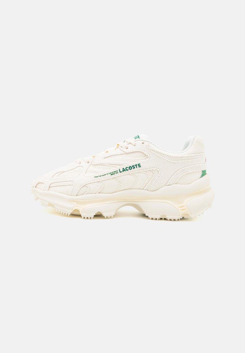 Chaussure de sport blanche avec un dessus en toile texturée, accents de lacets verts et semelle rembourrée présentant un motif de traction prononcé.
