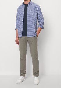 Blauw-witte geruite blouse, gecombineerd met een marineblauw T-shirt, kaki broek en witte sneakers. Casual outfit met knoopdetails op de blouse.