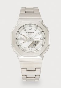 Montre Casio G-Shock argentée avec un cadran rond, affichage digital et analogique, bracelet en métal, boîtier texturé, et des fonctionnalités telles que WR 20BAR, alarme et lumière.