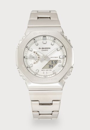 Stříbrné hodinky Casio G-Shock s kulatým ciferníkem, digitálním a analogovým displejem, kovovým páskem, texturovaným pouzdrem a funkcemi jako WR 20BAR, budík a osvětlení.