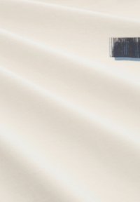 Lichtbeige stof met een gladde textuur, met een klein donkerblauw grafisch accent in de rechterbovenhoek.
