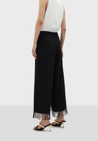 Svarta byxor med vida ben och fransdetalj vid fållen, slät textur, elastisk midja och två bakfickor; matchas med klacksandaler.