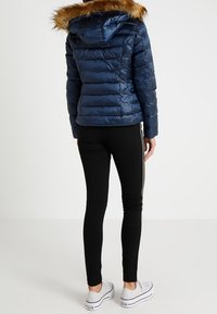 Laivastonsininen toppatakki tekoturkistupsulla varustetulla hupulla, tikattu vaakasuorilla saumoilla ja ribbineuloksella. Yhdistetty mustiin leggingsseihin ja valkoisiin tennareihin.