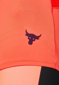 Tessuto sportivo corallo con una texture liscia presenta un logo scuro di un toro. Include dettagli cuciti e blocchi di colore in pesca e nero.