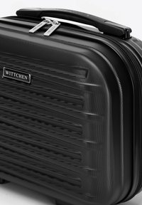 Valise rigide noire avec des lignes horizontales texturées, fermeture à double zip et une poignée robuste. Présente un logo de marque métallique.
