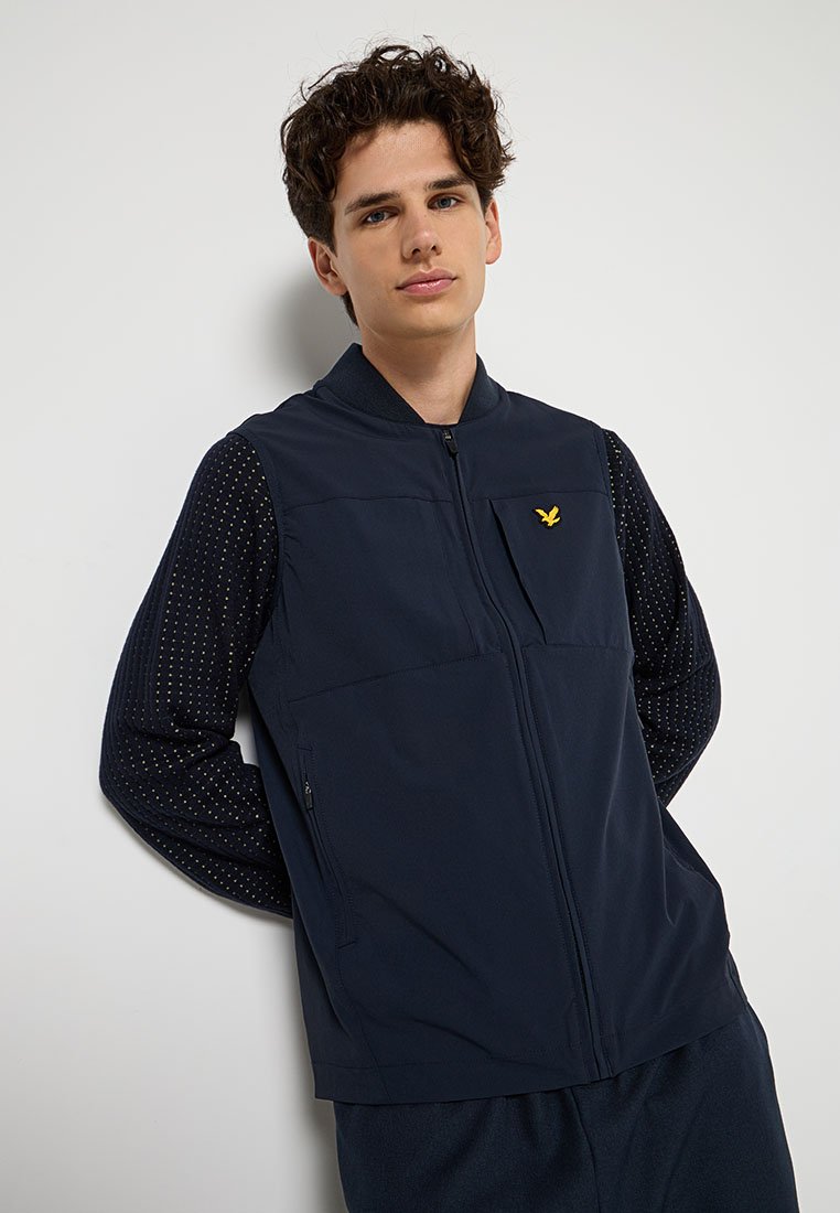 Gilet soft-shell bleu marine avec fermeture éclair à l'avant, poche poitrine et logo jaune. Caractérisé par des manches longues avec un motif de points texturé.
