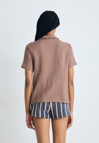 Chemise courte à manches courtes en brun texturé avec col, associée à un short rayé bleu marine. La vue de dos montre des manches courtes et une coupe décontractée.