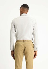 Langärmliges, hellgraues Hemd mit strukturiertem Finish und geknöpften Manschetten, kombiniert mit beigen Hosen mit elastischem Bund und Gesäßtaschen.