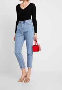 Schwarzes, geripptes Langarmoberteil, hoch geschnittene, hellblaue Jeans, beiger, Riemchen-Sandalen, roter Handtasche. Minimalistisches Design mit umgeschlagenen Bündchen.