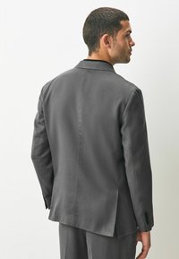 Grau Anzugjacke mit Reverskragen und einem Schlitz. Verfügt über glattes, strukturiertes Material und geknöpfte Bündchen. Die Rückansicht zeigt eine taillierte Passform.