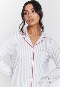 Gray and white striped pajama top with red piping, button closure, single chest pocket, long sleeves, and soft fabric texture.