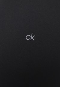 Tissu noir à texture lisse avec un petit logo brodé "ck" en blanc sur le côté inférieur droit.