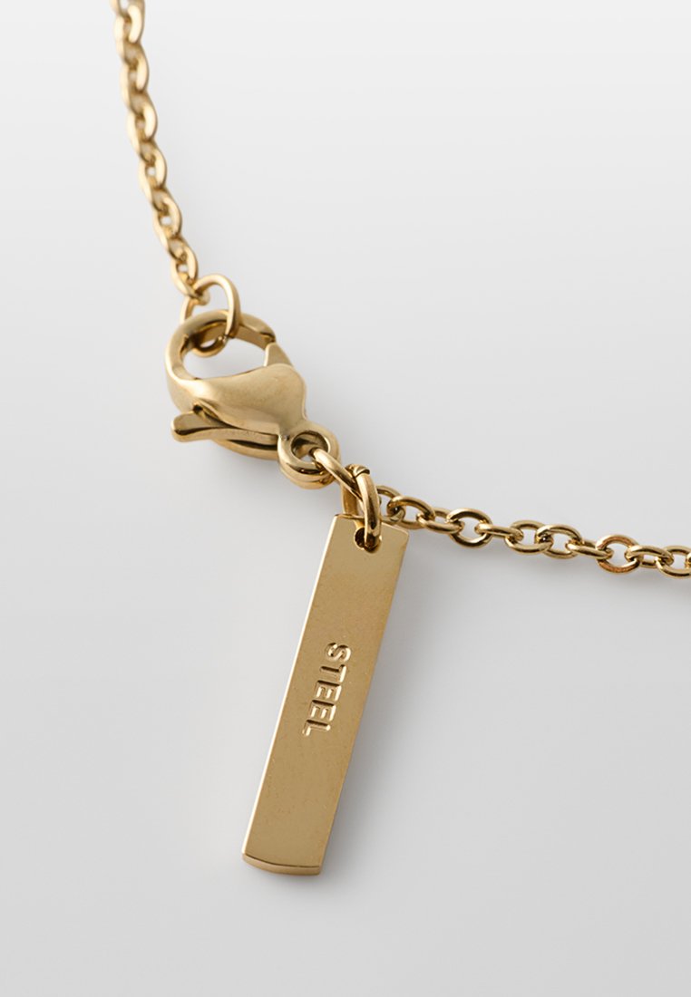 Halskette aus goldfarbenem Stahl mit einer kurzen, verlinkten Kette und einem rechteckigen Anhänger, auf dem das Wort "STEEL" eingraviert ist. Mit Karabinerverschluss.
