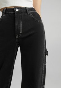 Svarta denimbyxor med vita sömmar, hög midja, rak passform och sidfickor med lockdetaljer. Matt textur.