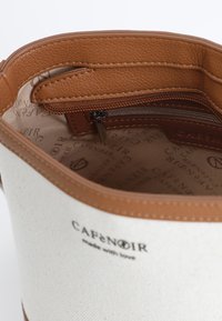 Vit canvasväska med brun läderdetalj och dragkedjeficka, med en logotyp tryckt på fodret och en slät yta.