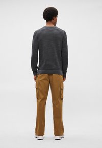 Ciemnoszara sweter z dzianiny z ściągaczami przy mankietach i u dołu, w połączeniu z jasnobrązowymi spodniami cargo z bocznymi kieszeniami i luźnym krojem. Białe sneakersy.