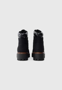Botas tobilleras negras con un exterior de ante, puntera redondeada, ribete de cuero negro brillante y una suela robusta con profundos surcos para mayor tracción.