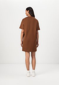 Bruine katoenen t-shirt jurk met een ontspannen pasvorm, korte mouwen en een ronde hals, die boven de knieën valt, gecombineerd met witte schoenen.