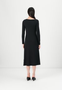 Robe noire à manches longues en matériau doux et extensible. Elle présente un design simple et ajusté avec une longueur mi-mollet et peu de détails.
