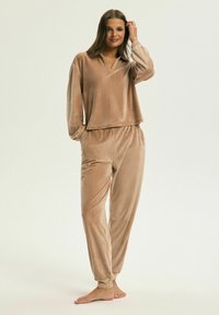 Zestaw dresowy z weluru w jasnobrązowym kolorze. Bluzka ma luźny krój z dekoltem w kształcie litery V, a spodnie mają elastyczny pas i tapered nogawki.