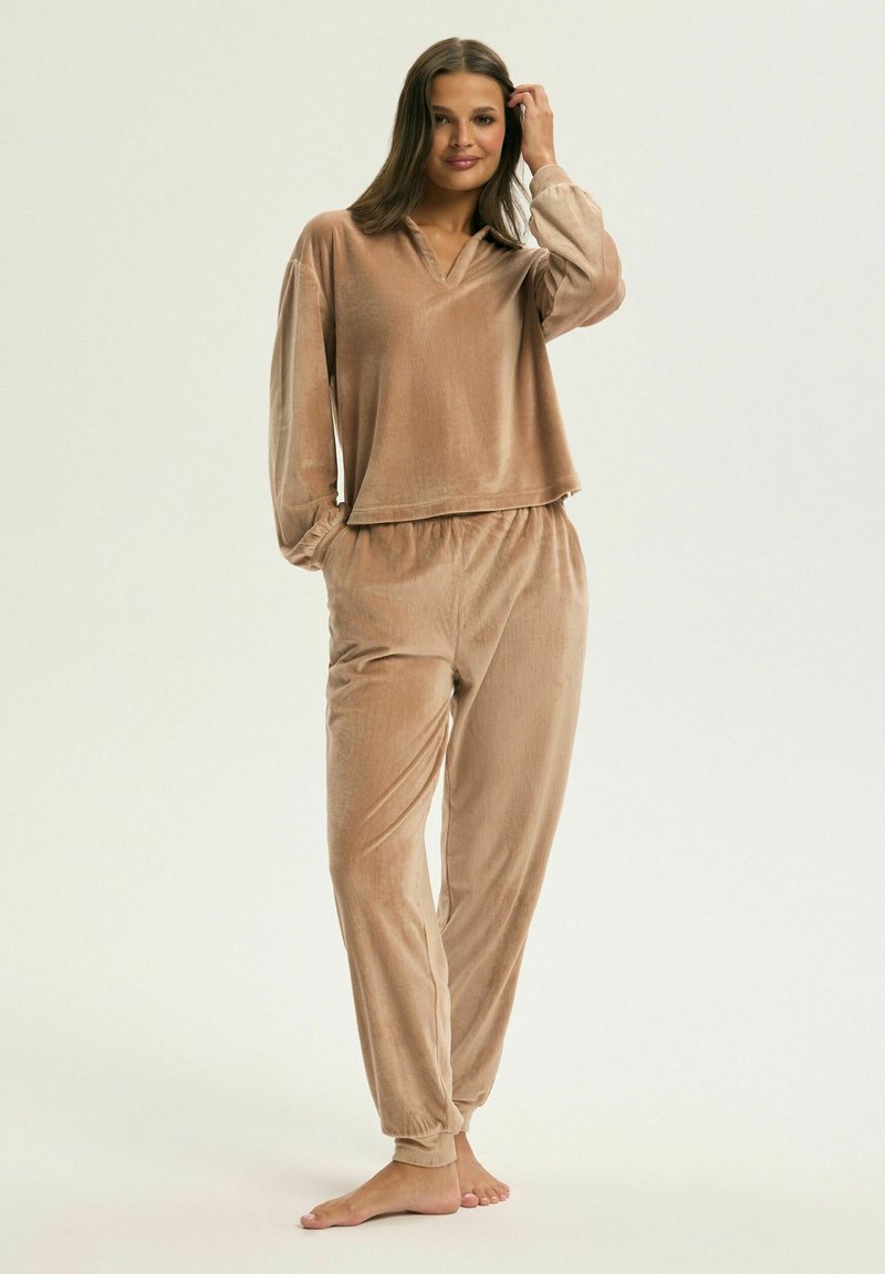Zestaw dresowy z weluru w jasnobrązowym kolorze. Bluzka ma luźny krój z dekoltem w kształcie litery V, a spodnie mają elastyczny pas i tapered nogawki.