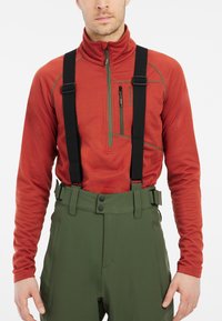 Haut en polaire rouge zippé avec des accents verts, associé à un pantalon de neige vert taille haute maintenu par des bretelles noires.
