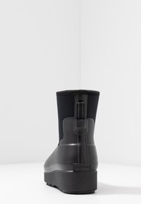 Botte de pluie noire mi-mollet avec languette et semelle texturée, marquée "Hunter" au niveau du talon, vue de l'arrière sur une surface blanche.