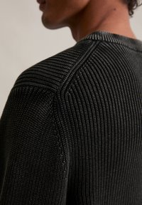 Černý strukturovaný pletený svetr s kulatým výstřihem, který má jemnou texturu a podrobné prošívání podél ramenních švů.