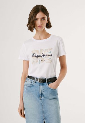 T-shirt bianca in cotone con logo "Pepe Jeans London" in blu navy e toni terreni, abbinata a una gonna di jeans azzurri e una cintura nera con borchie.