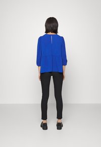 Top blu reale con maniche a sbuffo, schiena a chiave, abbinato a pantaloni neri slim-fit e scarpe con piattaforma. Tessuto morbido, design casual.