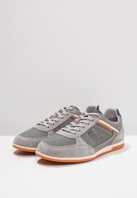 Grå sneakers med en kombination av mocka och mesh-material, orangea randiga detaljer och en lättviktsdesign med gummisulor.