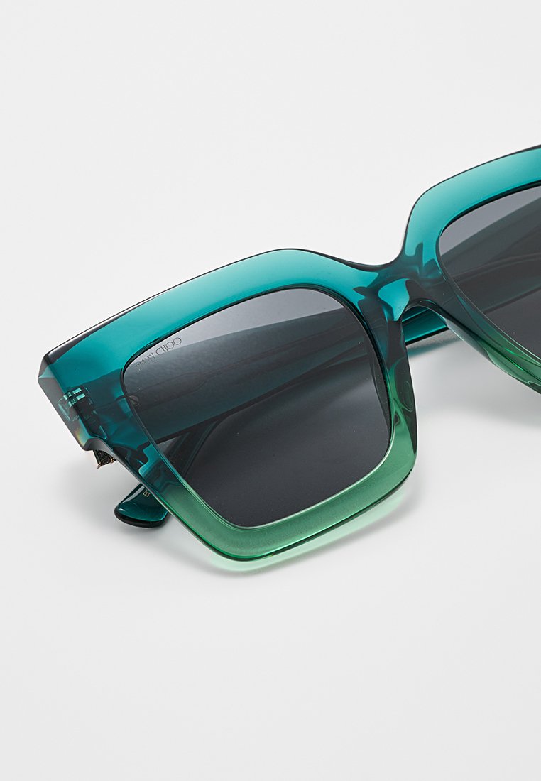 Une paire de lunettes de soleil surdimensionnées avec un design dégradé, présentant une monture en plastique translucide allant du vert foncé au vert clair et des verres sombres.