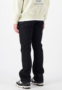 Zwarte cargo broek gemaakt van stevige stof, met zijzakken, een rechte pasvorm en contrasterende witte stiksels.