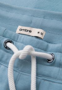 Pantalones cortos azul claro con una cinturilla texturizada, cordón blanco y un ojete negro, que presentan una etiqueta "ombre" que indica la talla M.