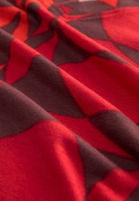 Red and dark brown patterned fabric with a soft texture, featuring curved shapes and a smooth drape, highlighting the vibrant color contrast.