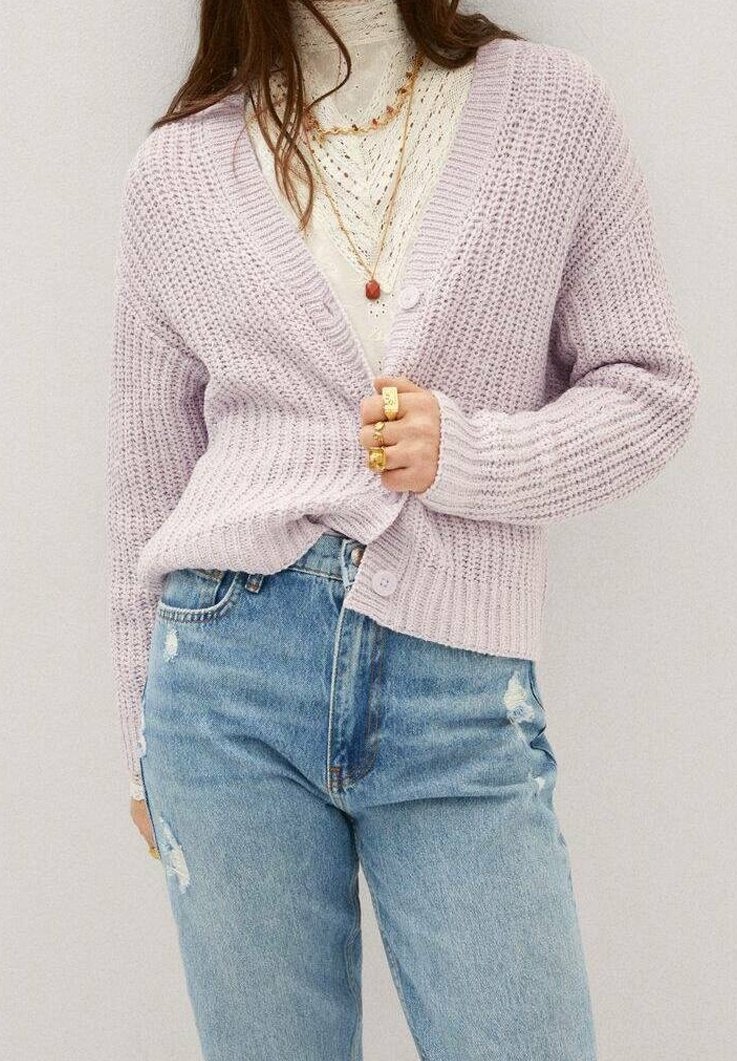 Cardigan en maille lavande avec texture côtelée, devant ouvert et deux boutons. Porté sur un haut crème à motif en dentelle et associé à un jean bleu déchiré.