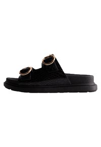 Sandales noires avec un motif texturé de serpent, ornées de deux accents circulaires dorés et d'une semelle noire épaisse pour le maintien.