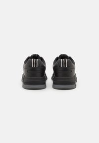 Sorte sneakers med to vertikale hvide striber på hælen, lavet af glat syntetisk materiale, med en tekstureret sål og polstret krave.