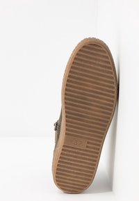 Olivgrön stövel med en räfflad brun gummisula, med en subtil dragkedjedetalj. Storlek 37 är präglad på sidan av sulan.