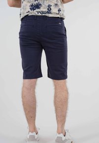 Shorts en coton bleu marine avec passants de ceinture et deux poches arrière. Longueur légèrement au-dessus du genou. Finitions des ourlets et des coutures soignées.