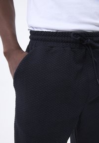 Joggers de color azul marino con textura, con cintura elástica, cordón ajustable y bolsillos laterales. El material presenta un patrón tejido único.