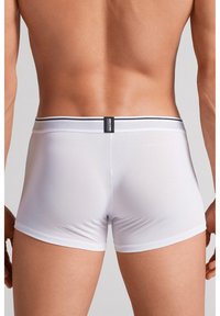 Naakte rug en taille van een man, gekleed in strakke witte boxershorts met een tailleband met zwarte strepen en een label aan de achterkant.