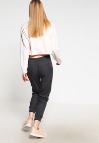 Kort ljusrosa sweatshirt och mörkgrå joggers med elastisk midja, ihop med beige skor. Slät tygkvalitet och avslappnad passform.
