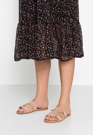 Beige mokkasaappaat, joissa on repaleiset hihnat, litteä pohja ja avoin kärki, yhdistetty kukkakuosiseksi mustaksi mekoksi.