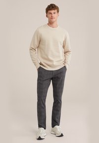 Lichtbeige longsleeve sweatshirt gecombineerd met donkergrijze ruitvormige broek en witte sneakers. Casual fit met een ronde hals.